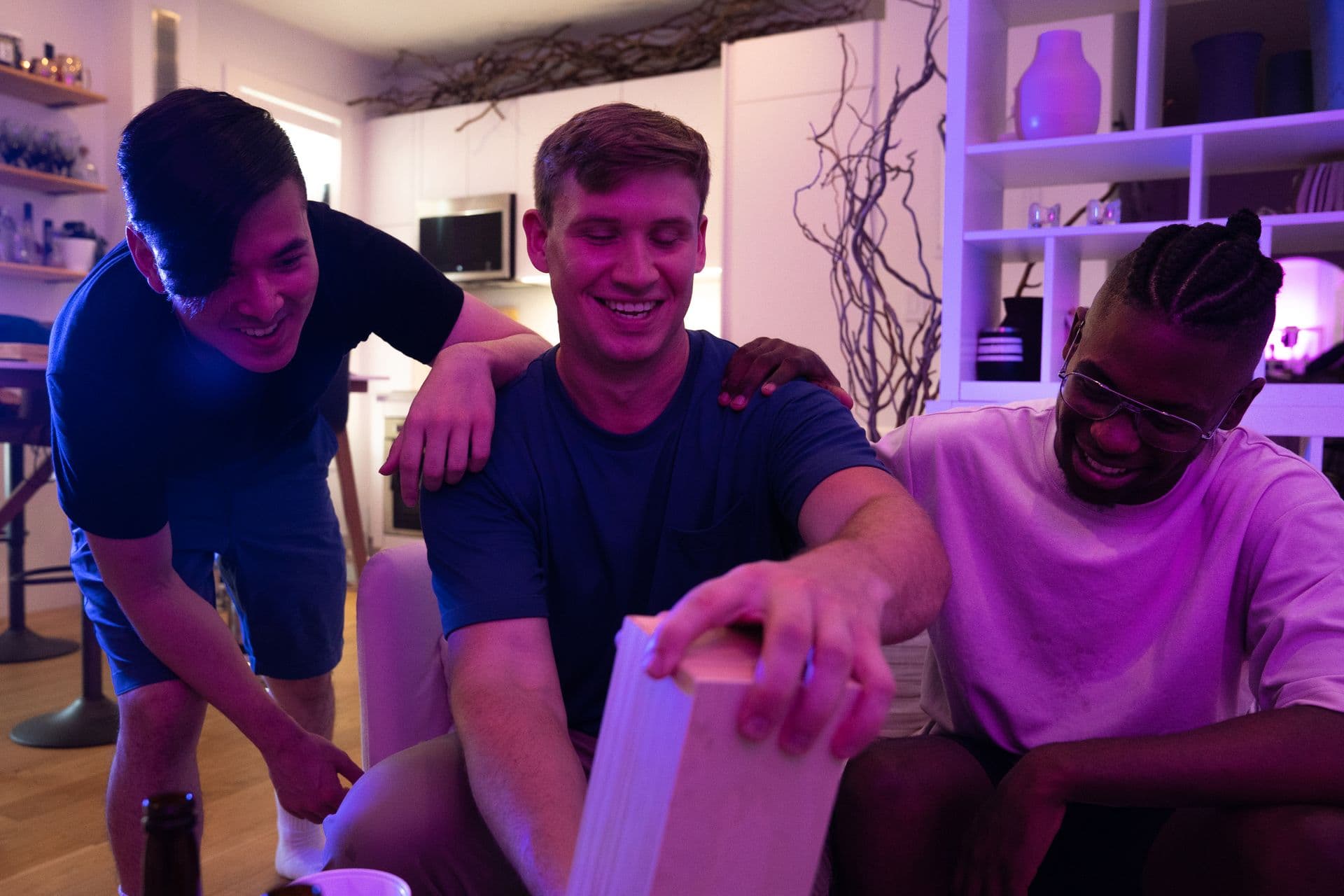 Three men laughing together over a board game at a games night.